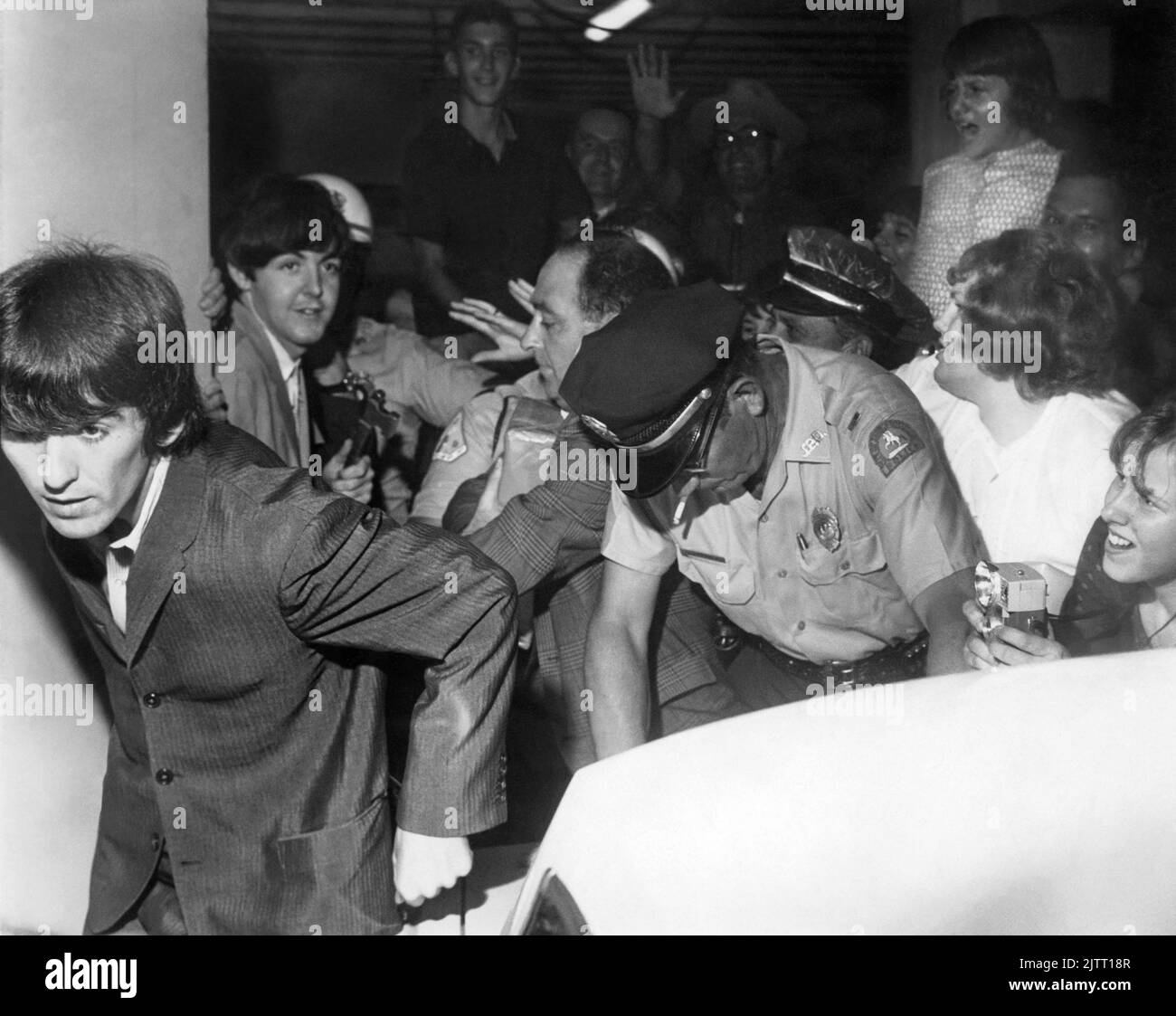 Les Beatles (George Harrison en premier plan et Paul McCartney derrière lui) quittent l'hôtel George Washington avec la police essayant de contrôler les fans pressés alors que le groupe se dirigeait vers leur concert Gator Bowl à Jacksonville, Floride, sur 11 septembre 1964. (ÉTATS-UNIS) Banque D'Images