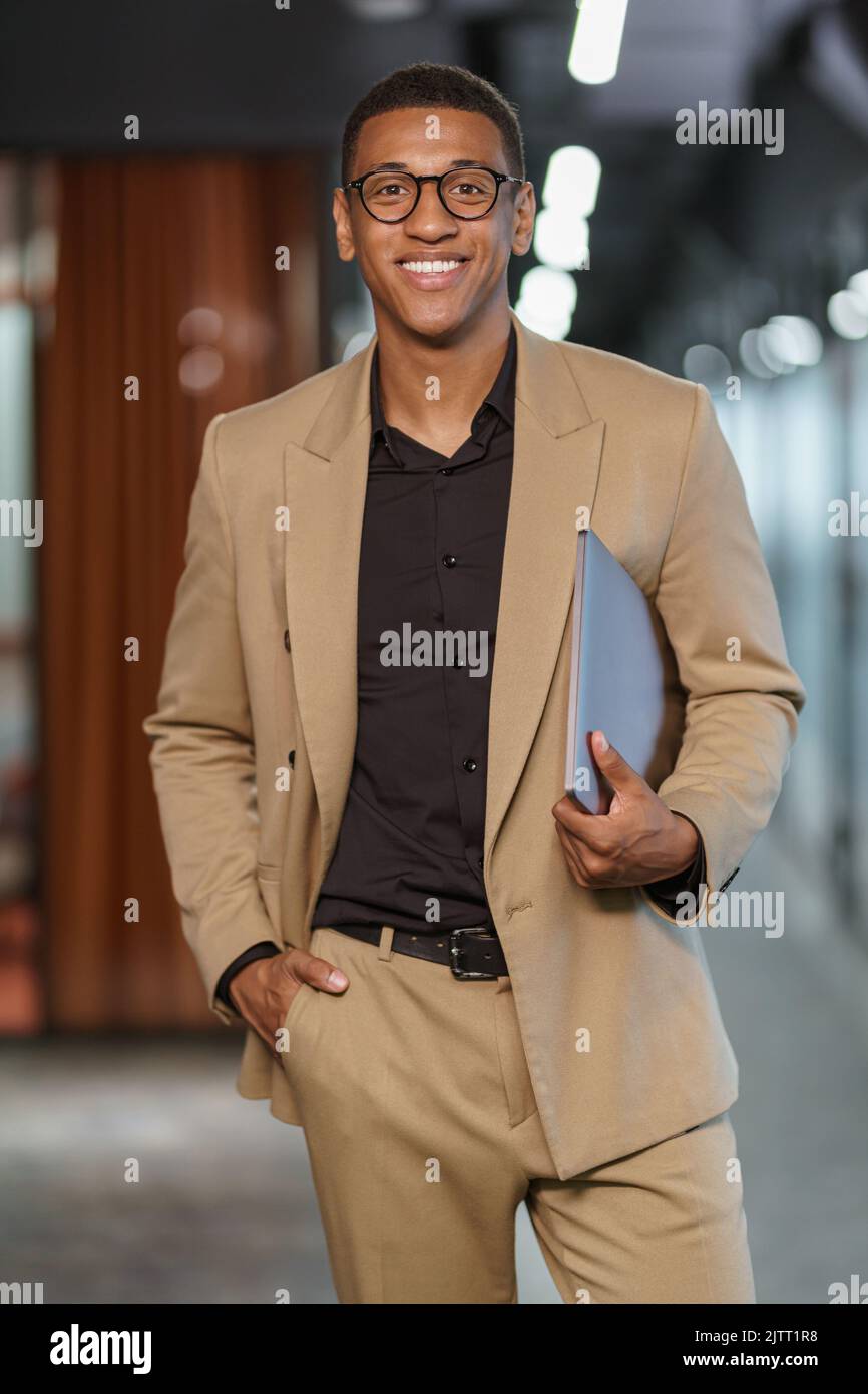 Beau homme d'affaires africain souriant avec des documents debout dans un collègue moderne Banque D'Images