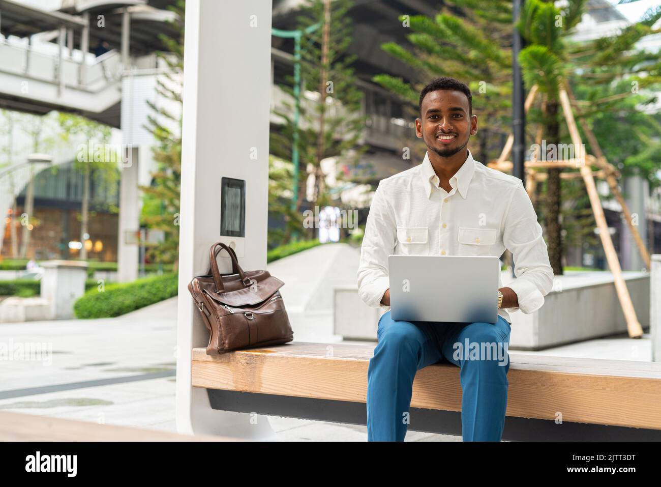 Portrait d'un jeune beau homme noir élégant utilisant un ordinateur portable en ville Banque D'Images