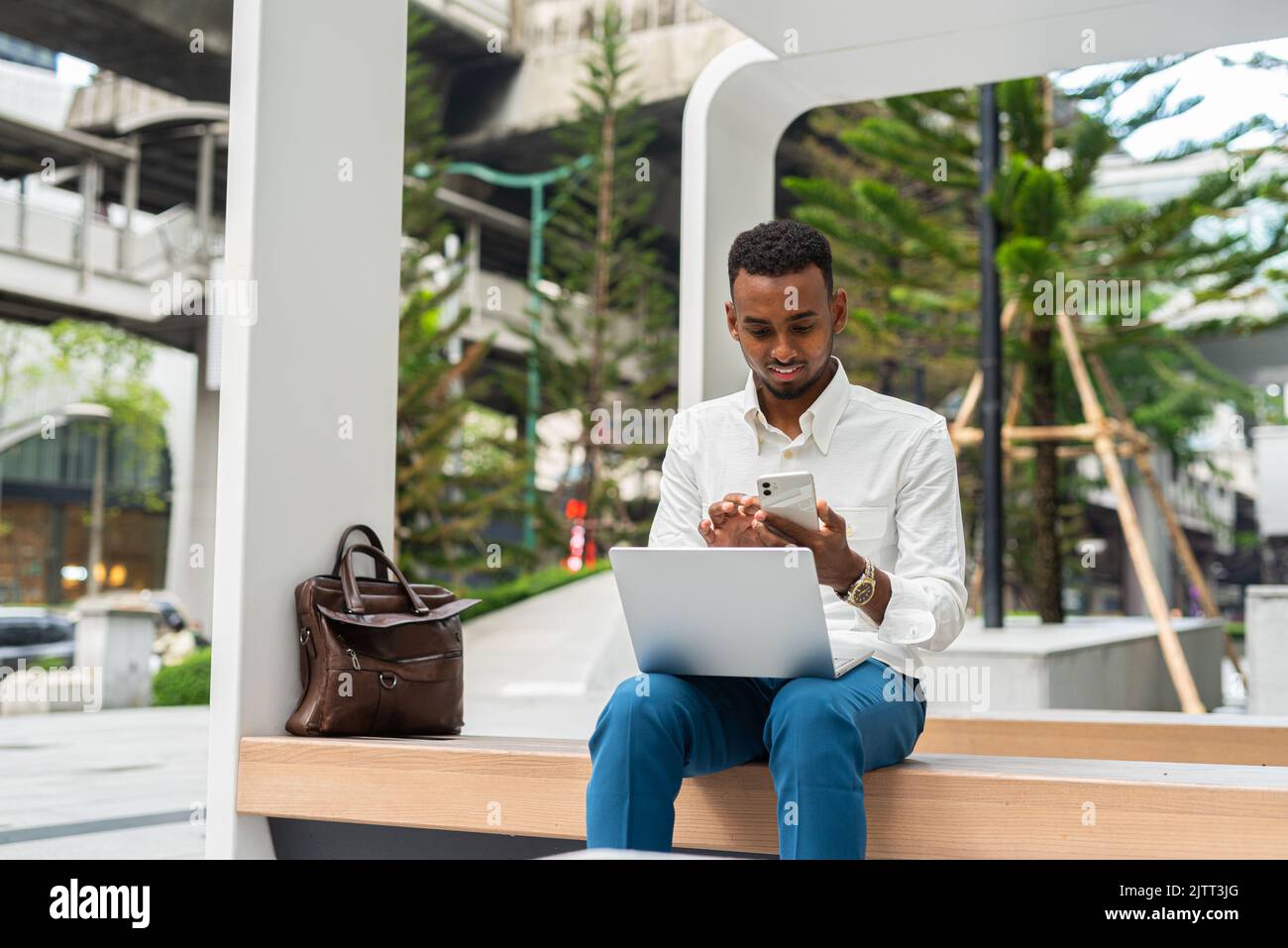 Portrait d'un jeune beau homme noir élégant utilisant un ordinateur portable en ville Banque D'Images