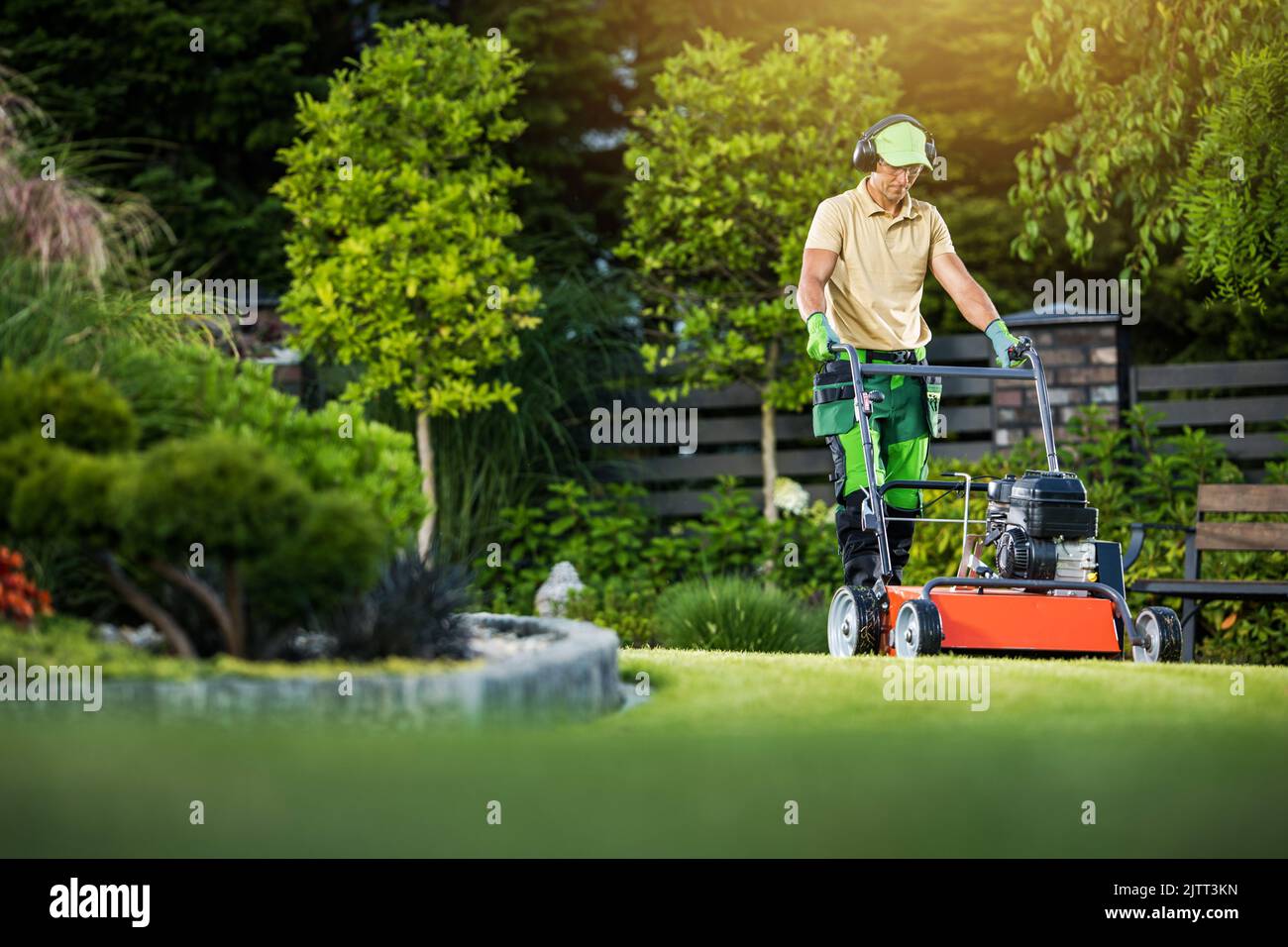 Paysagiste caucasien professionnel portant un casque de travail uniforme et de sécurité tonte de la pelouse dans le jardin paysagé d'arrière-cour à l'aide de Wal à essence Banque D'Images