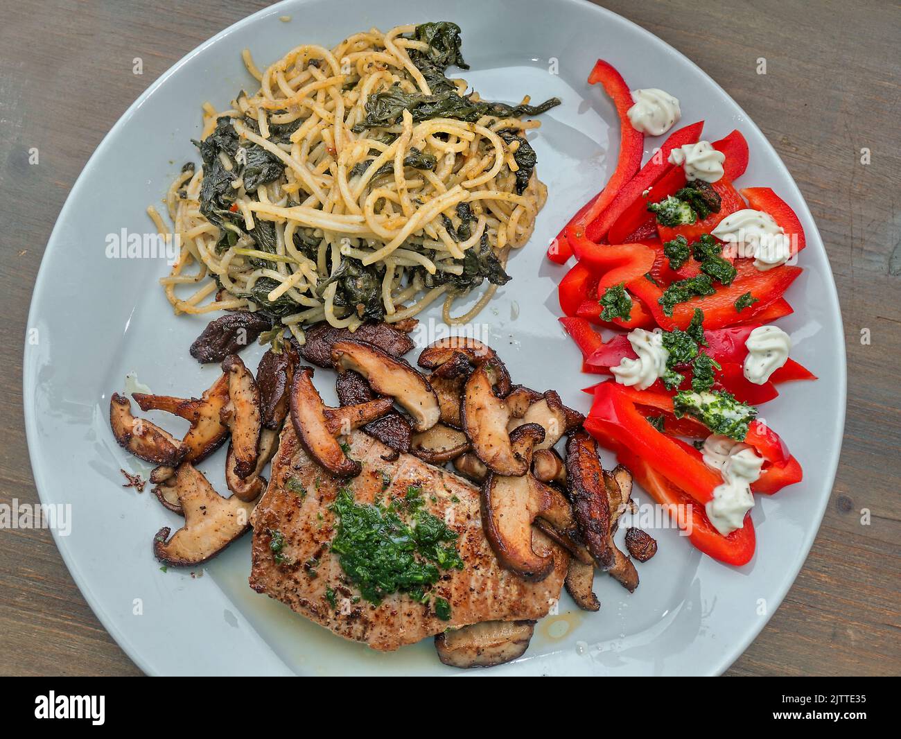 Vue de dessus d'une assiette à dîner gris clair avec thon poêlé, champignons shiitake rôtis, spaghetti avec câpres et feuilles d'épinards, et poivron rouge cru Banque D'Images