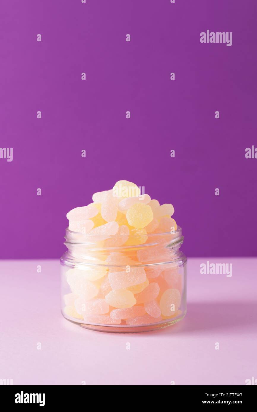 Gros plan des bonbons gélifiés dans un pot en verre sur fond violet. Vue avant, mise au point sélective, espace de copie. Banque D'Images