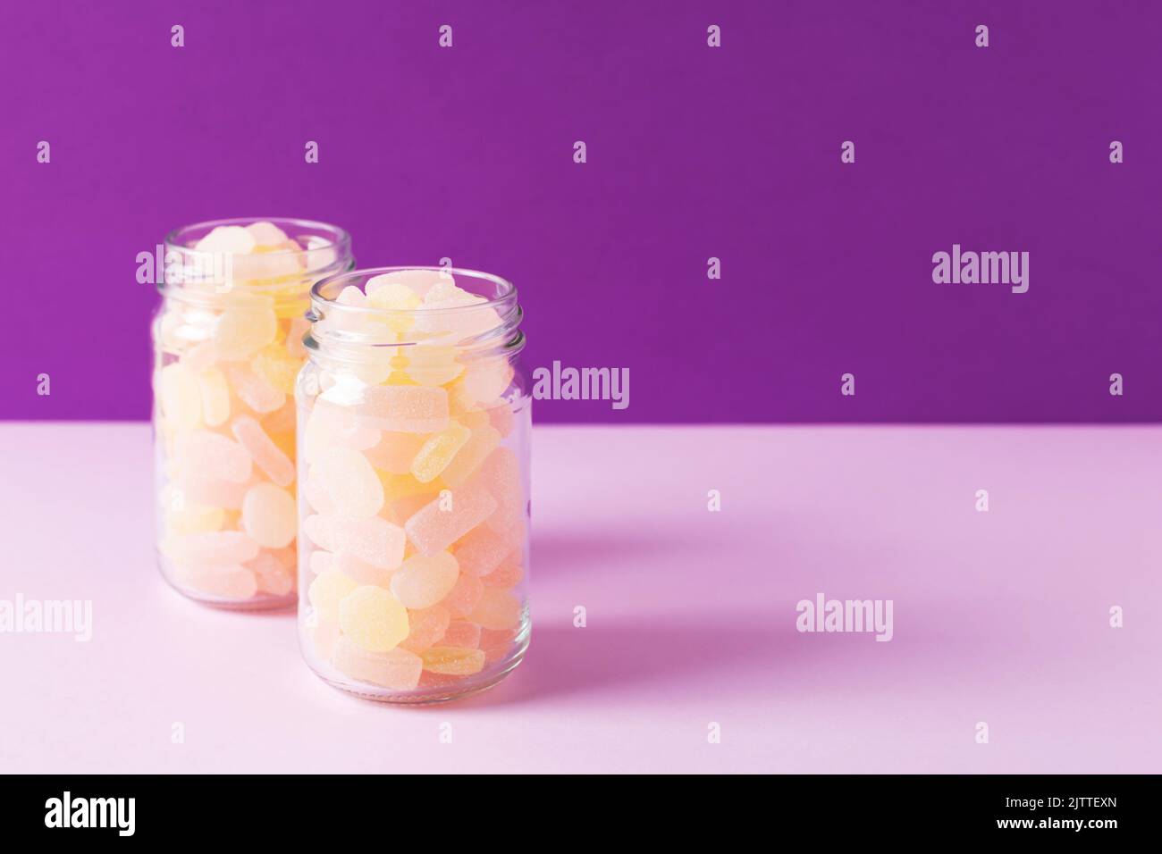 Gros plan de deux bocaux en verre remplis de bonbons gélifiants aux agrumes sur fond violet. Prise de vue en studio, mise au point sélective, espace pour le texte. Banque D'Images