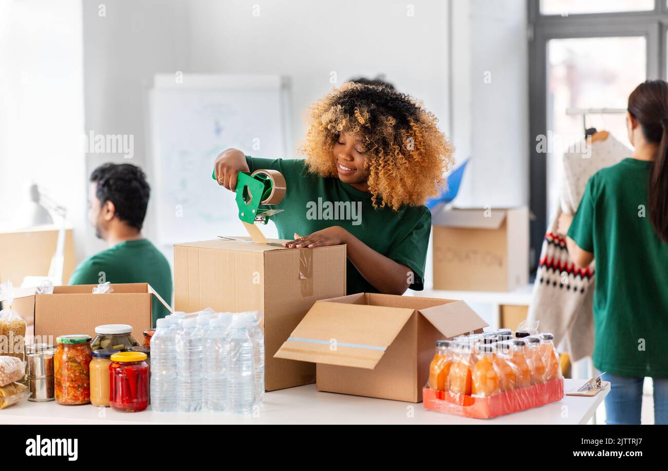 des bénévoles heureux emballant des aliments dans des boîtes de dons Banque D'Images