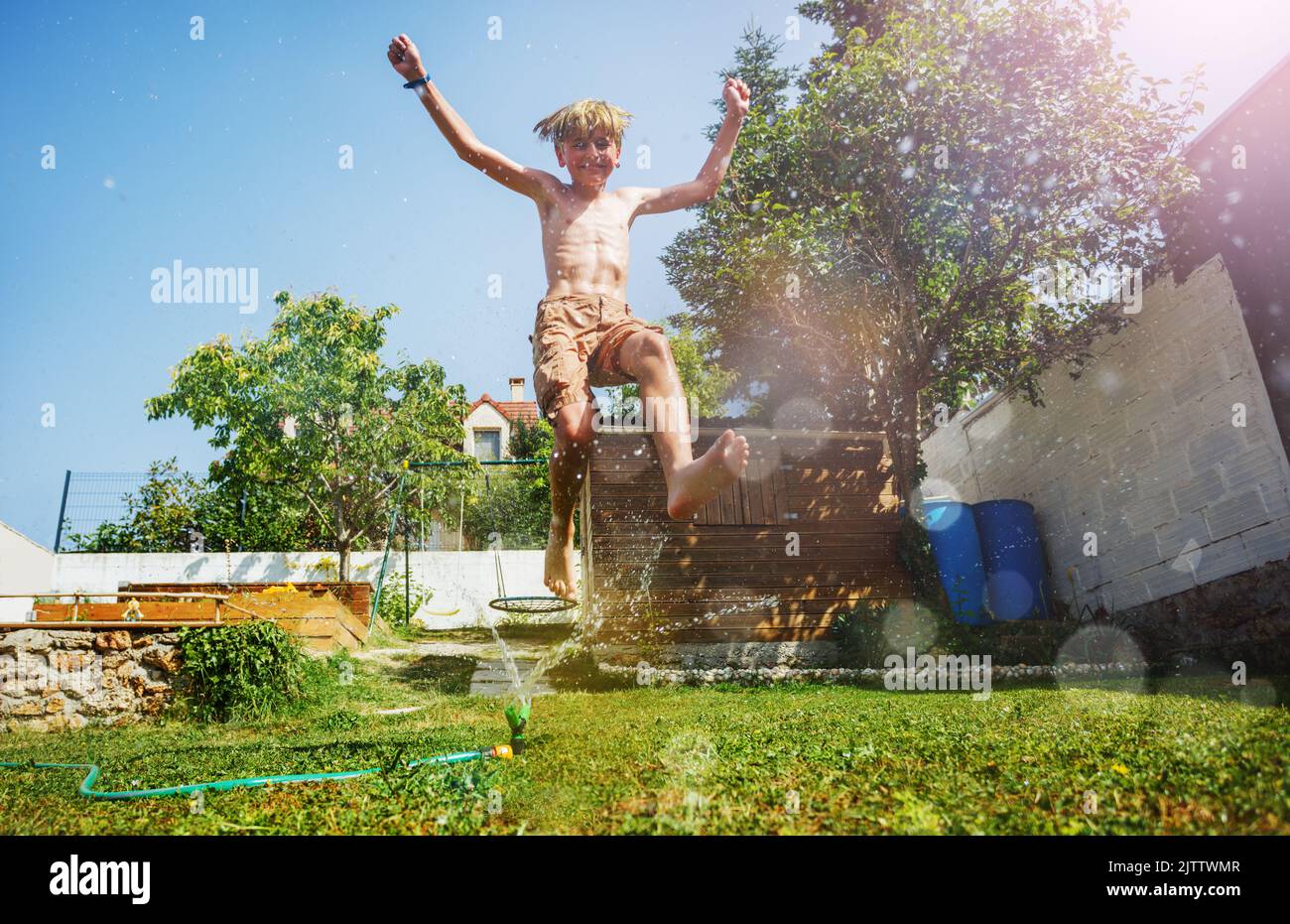 Bonhomme sautez au-dessus de l'arroseur d'eau avec les mains vers le haut sur la pelouse du jardin Banque D'Images