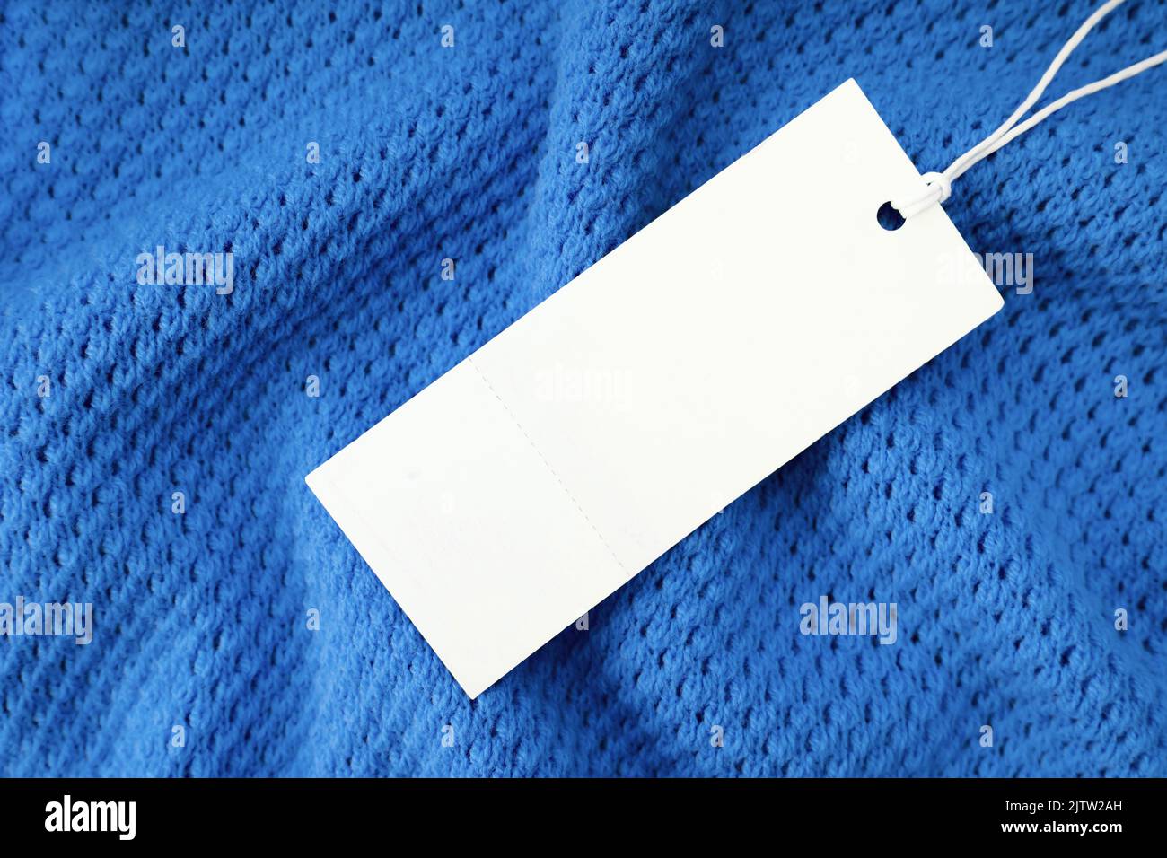 Blanc blanc vierge rectangulaire étiquette de vêtement, modèle de maquette d'étiquette sur fond de tissu tricoté bleu . Étiquette de prix avec espace pour le texte. Shopping, australie méridionale Banque D'Images