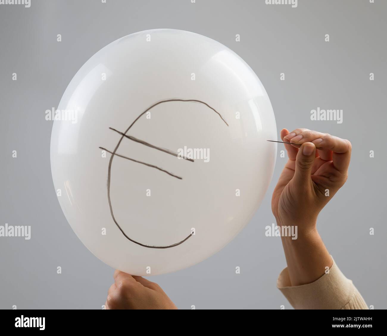 Une femme éclate avec une aiguille un ballon avec l'inscription euro. Banque D'Images
