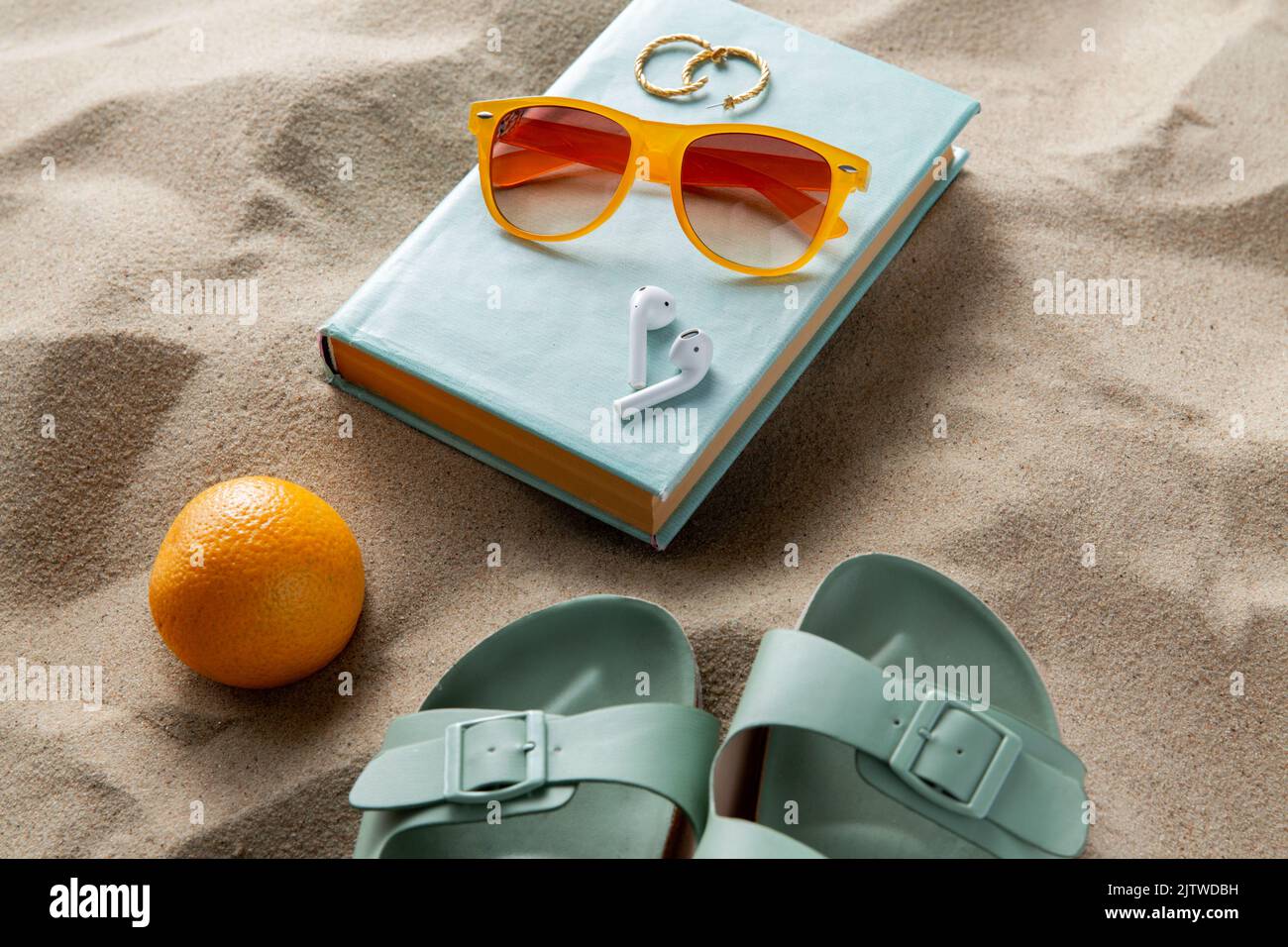 chaussons, orange, oreillettes et lunettes de soleil sur la plage Banque D'Images