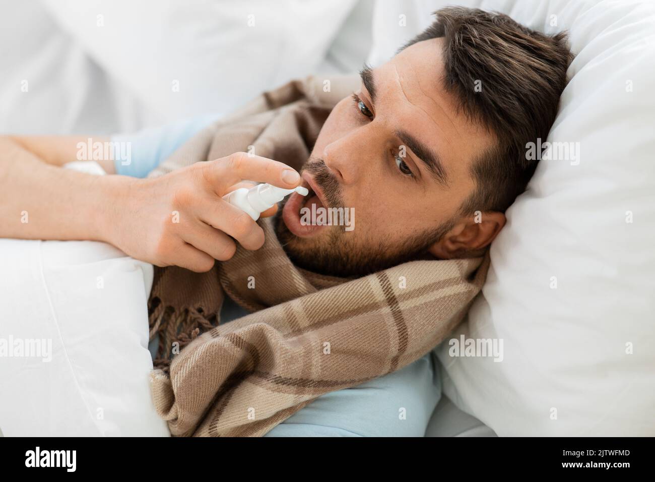 homme malade avec un spray oral couché dans le lit à la maison Banque D'Images