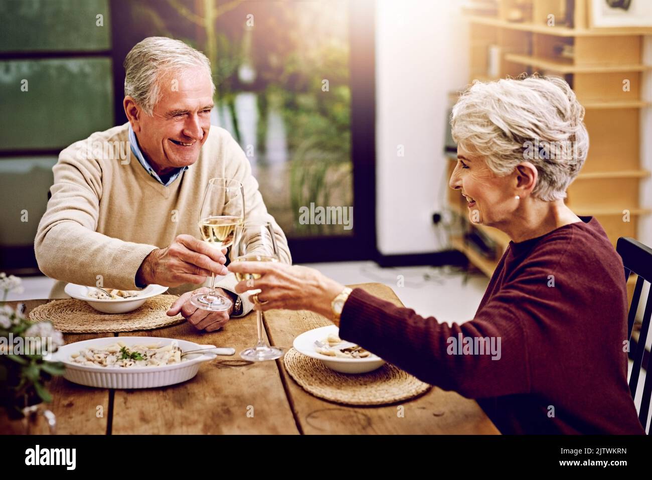 Que nous avons beaucoup plus d'années ensemble. Un couple de personnes âgées toasting avec des verres à vin pendant qu'ils aiment un repas à la maison. Banque D'Images