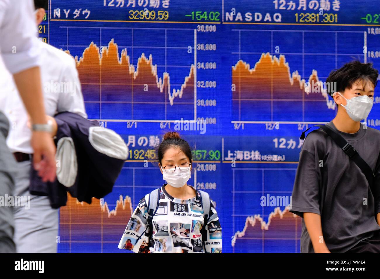 Tokyo, Japon. 24th août 2022. Les personnes portant des masques de visage marchent devant un écran affichant les indices boursiers de Nikkei en moyenne et mondiaux en dehors d'une maison de courtage, dans le cadre de la pandémie du coronavirus à Tokyo. Crédit : SOPA Images Limited/Alamy Live News Banque D'Images