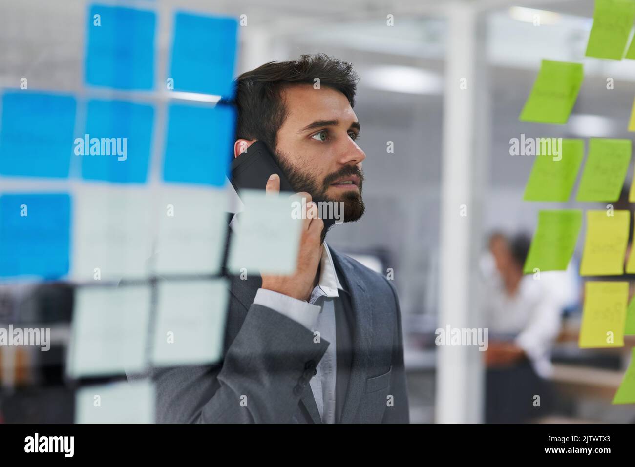 Je ne regarde pas le plan pendant que nous parlons... un jeune homme d'affaires qui parle au téléphone tout en regardant des notes sur un mur de verre. Banque D'Images