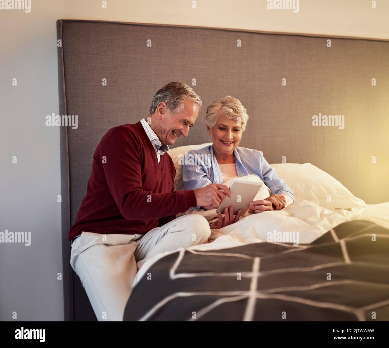 La technologie nous simplifie la vie. Un couple senior regarde une tablette ensemble tout en étant assis au lit. Banque D'Images