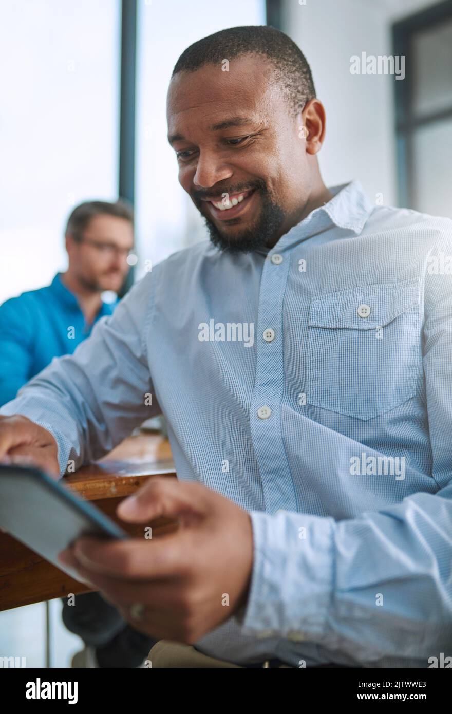 HES est satisfait de sa nouvelle ressource. Un homme d'affaires utilisant sa tablette avec un collègue en arrière-plan. Banque D'Images
