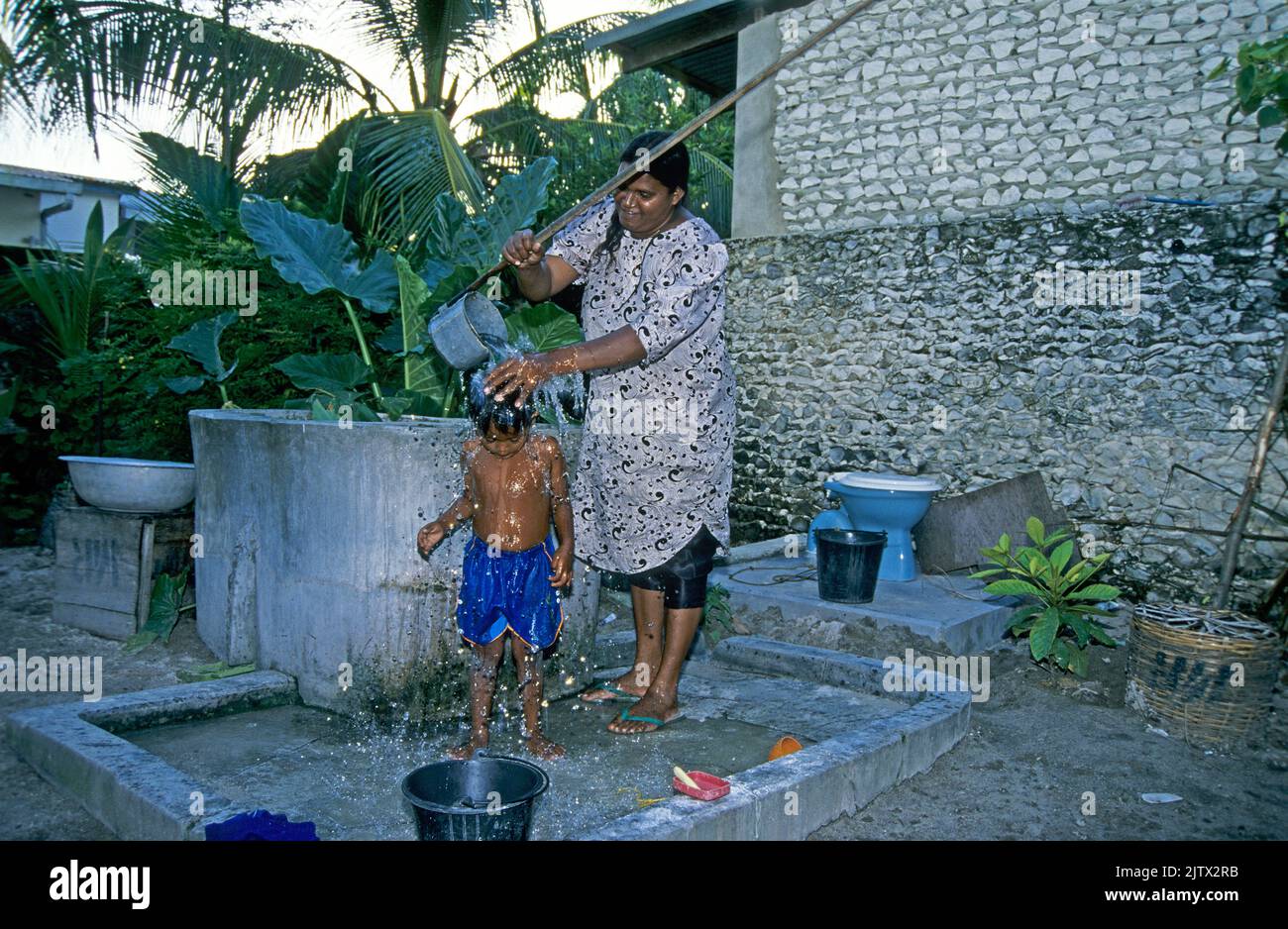 La femme maldivienne passe une douche à son fils, île d'origine Mahembadhoo, Maldives, océan Indien, Asie Banque D'Images