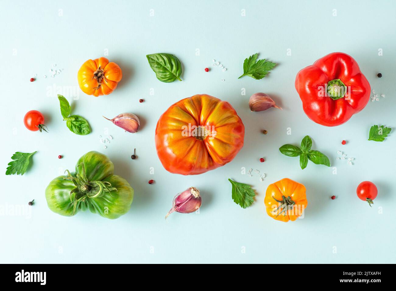 Composition des aliments. Tomates, basilic, ail et poivre sur fond bleu pastel. Pose à plat. Vue de dessus. Motif de légumes Banque D'Images