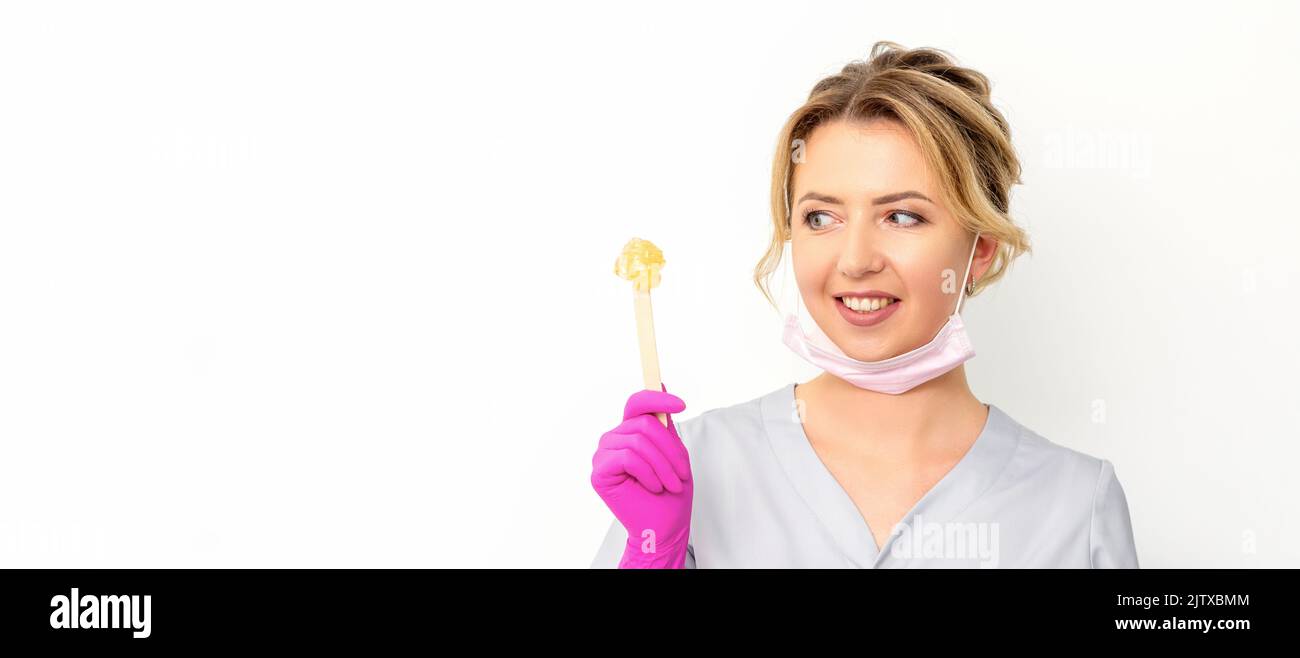 Le maître de l'enlèvement de cheveux de sucre contient de la pâte de sucre jaune liquide, de la cire pour l'épilation sur un bâton de bois sur un fond blanc Banque D'Images