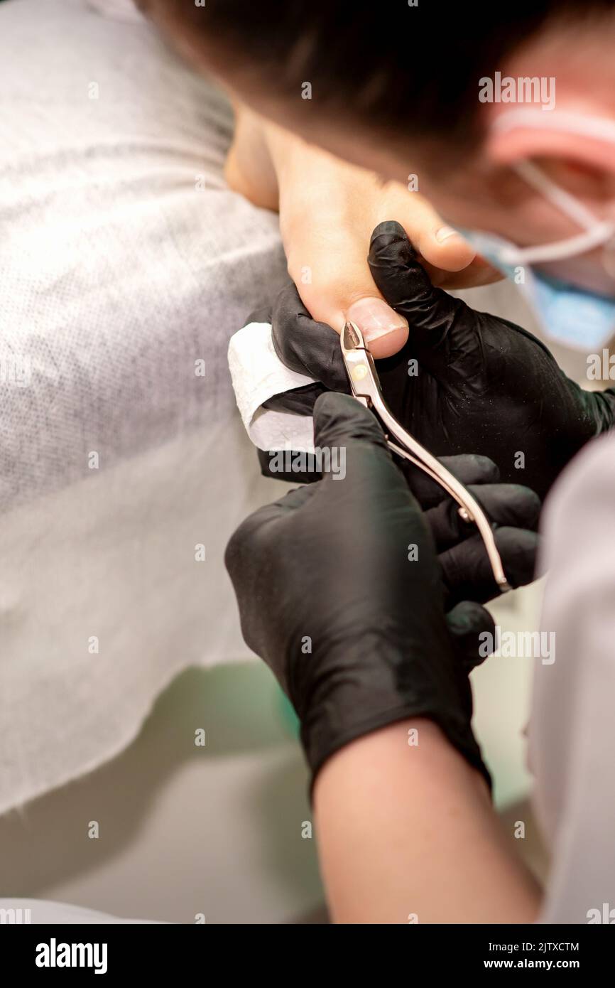 Pédicure professionnelle. Pédicure maître portant des gants en latex coupe les ongles du pied féminin dans le salon de beauté, gros plan Banque D'Images