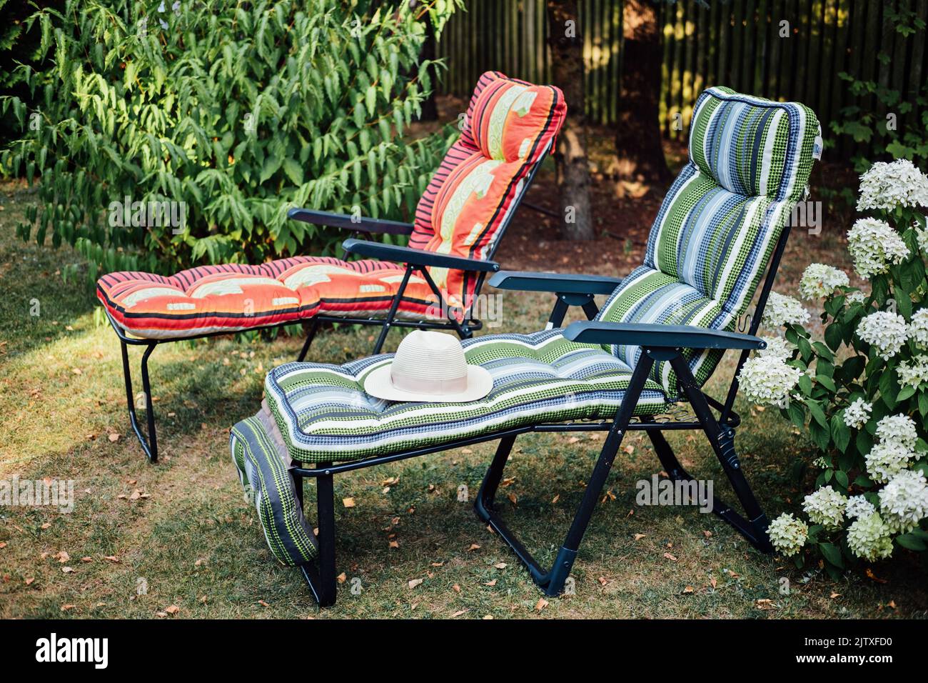 Deux chaises longues avec chapeau de paille dans la cour intérieure. Deux chaises longues vides dans un jardin ensoleillé pour la détente. Banque D'Images
