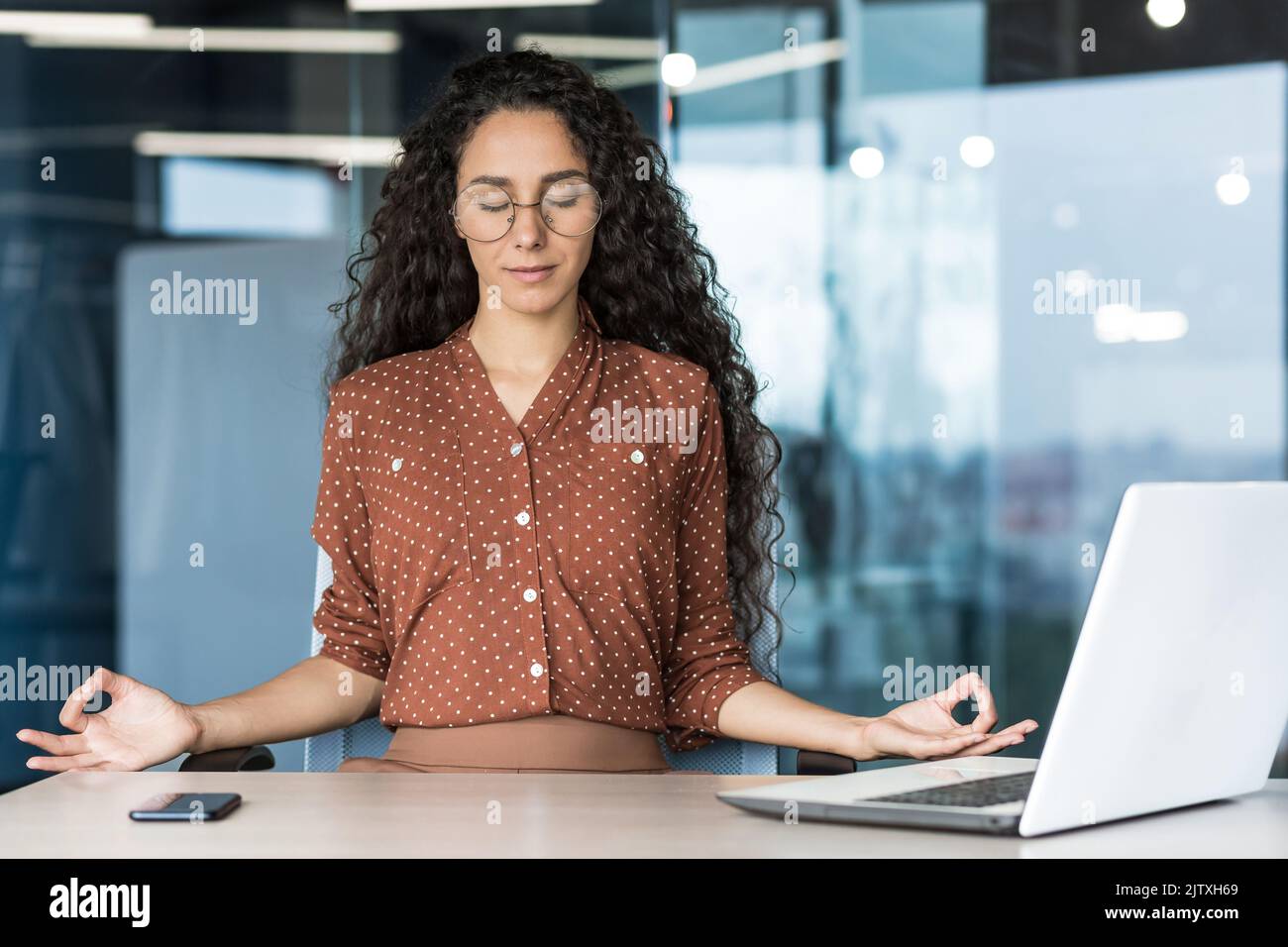 Jeune beau développeur web hispanique travaillant à l'intérieur d'un immeuble de bureau, femme se reposant méditant sur le lieu de travail avec les yeux fermés, femme employée utilisant un ordinateur portable pour écrire du code. Banque D'Images