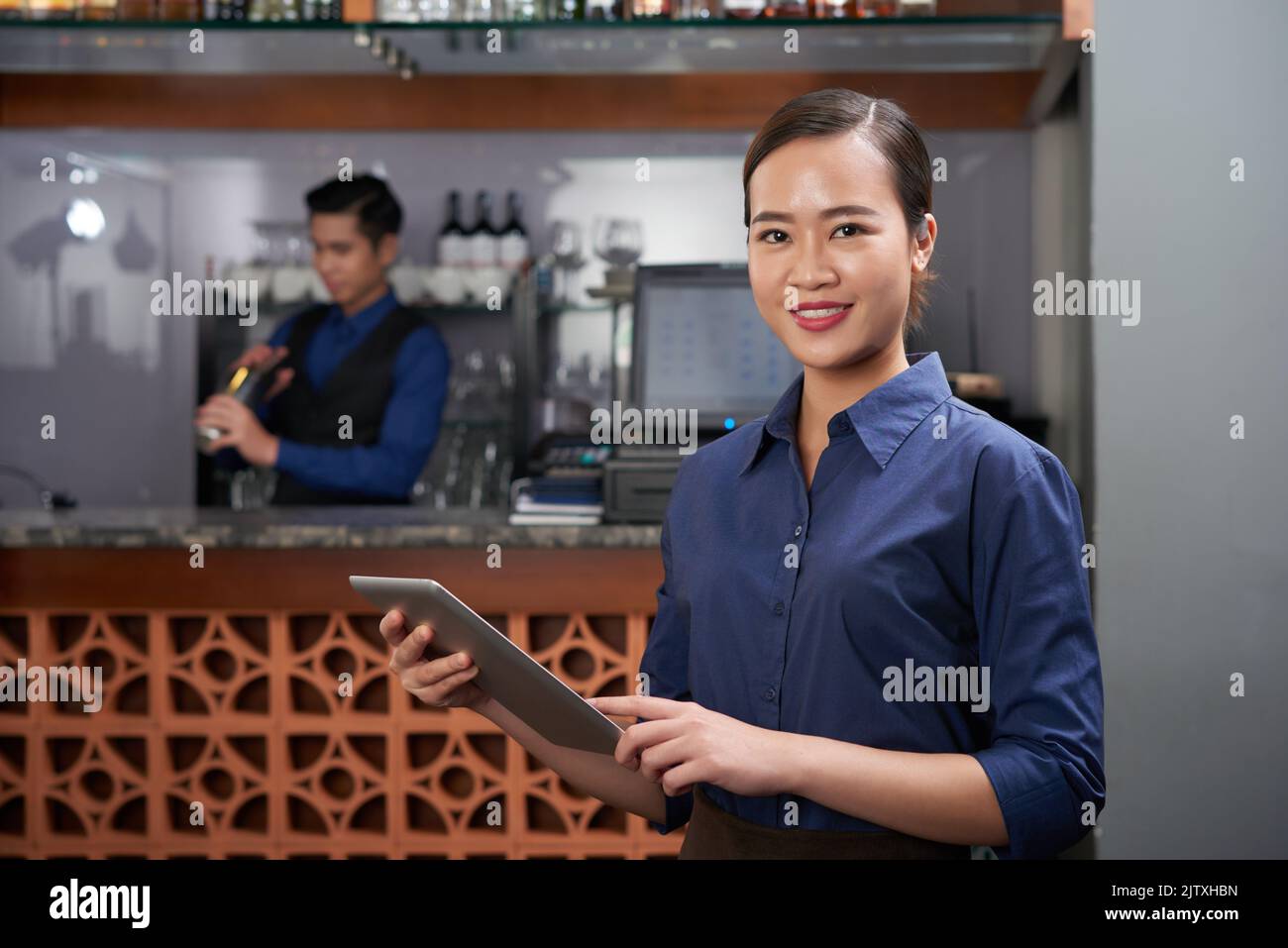 Jolie propriétaire de barre vietnamienne avec un ordinateur de tablette dans ses mains Banque D'Images