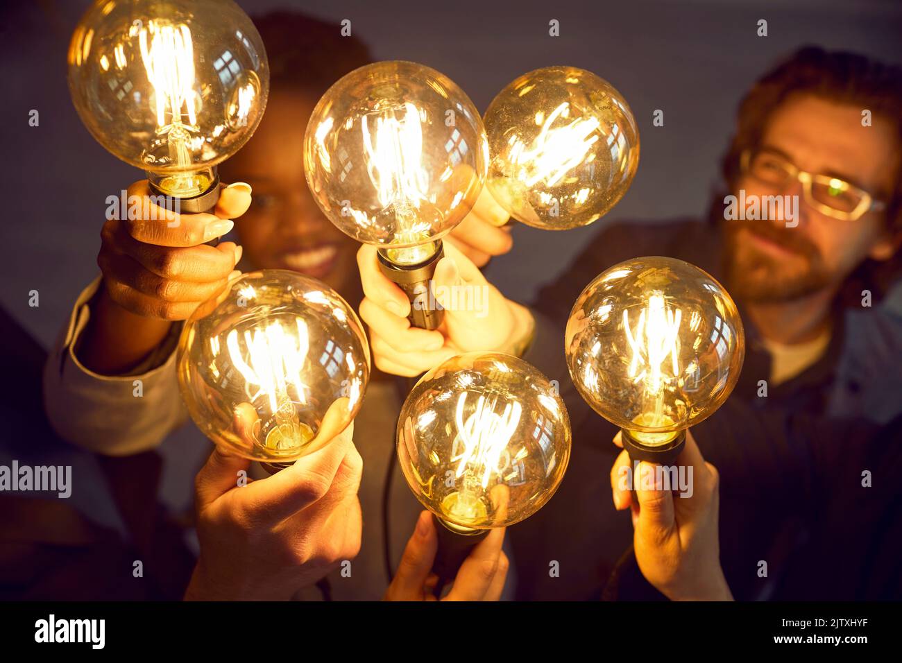 Des collègues joyeux tiennent ensemble des ampoules lumineuses comme symbole d'une nouvelle idée commerciale. Banque D'Images