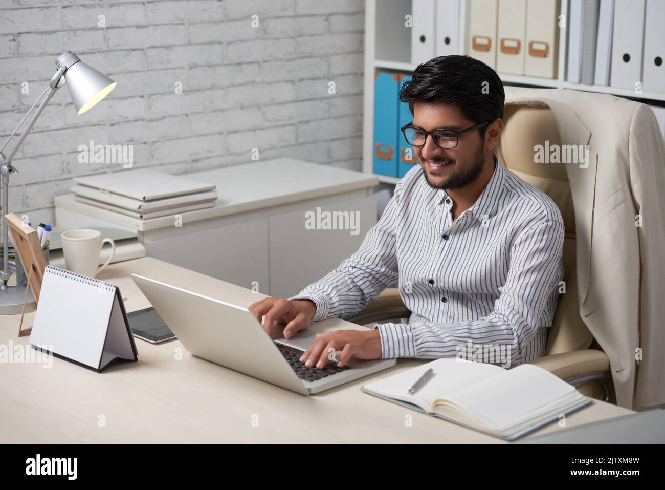 Un propriétaire indien souriant travaillant sur un ordinateur portable dans son bureau Banque D'Images