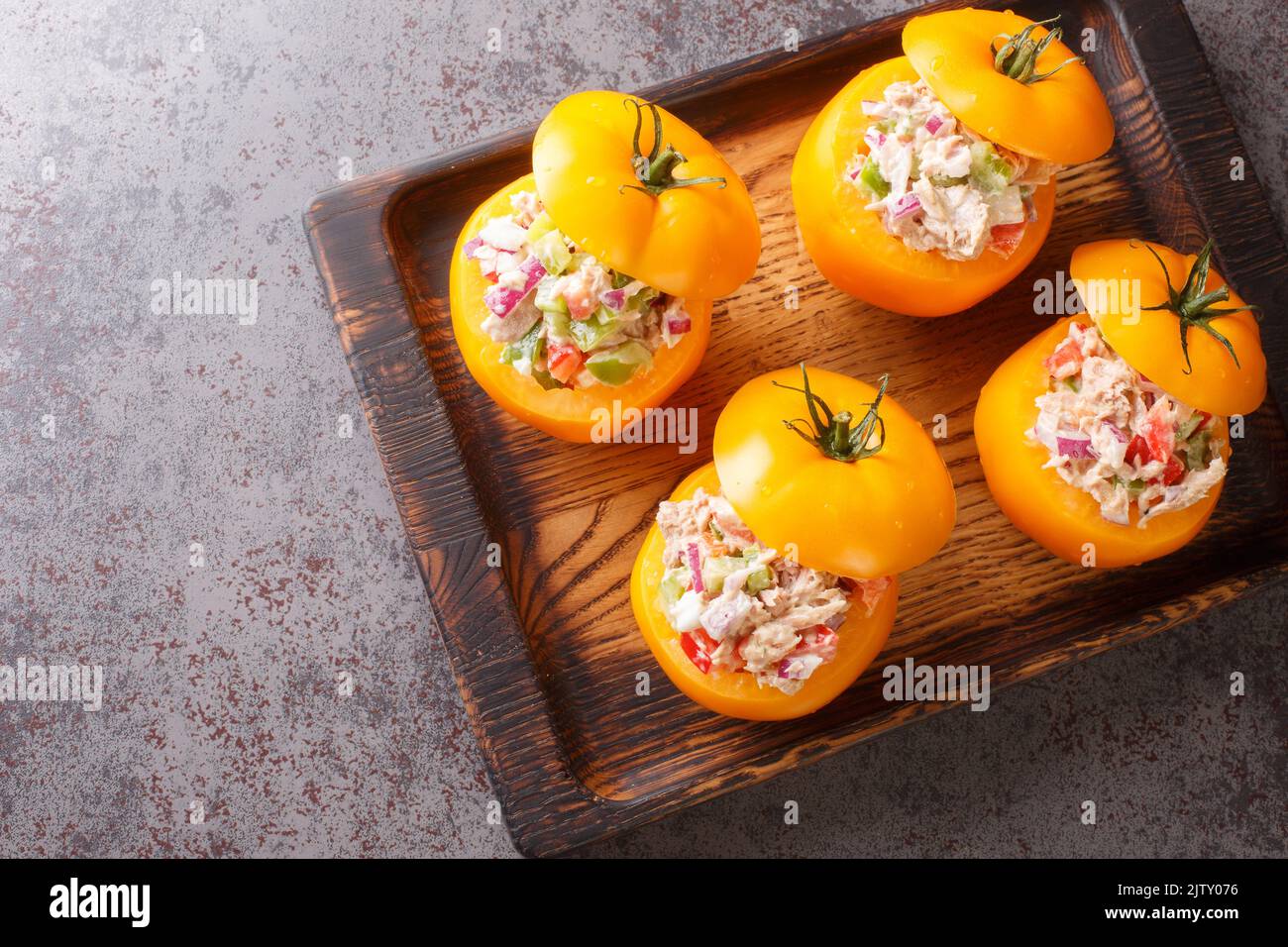 Délicieux hors-d'œuvre tomates jaunes farcies avec salade de thon et légumes gros plan sur un plateau en bois sur la table. Vue horizontale du dessus Banque D'Images