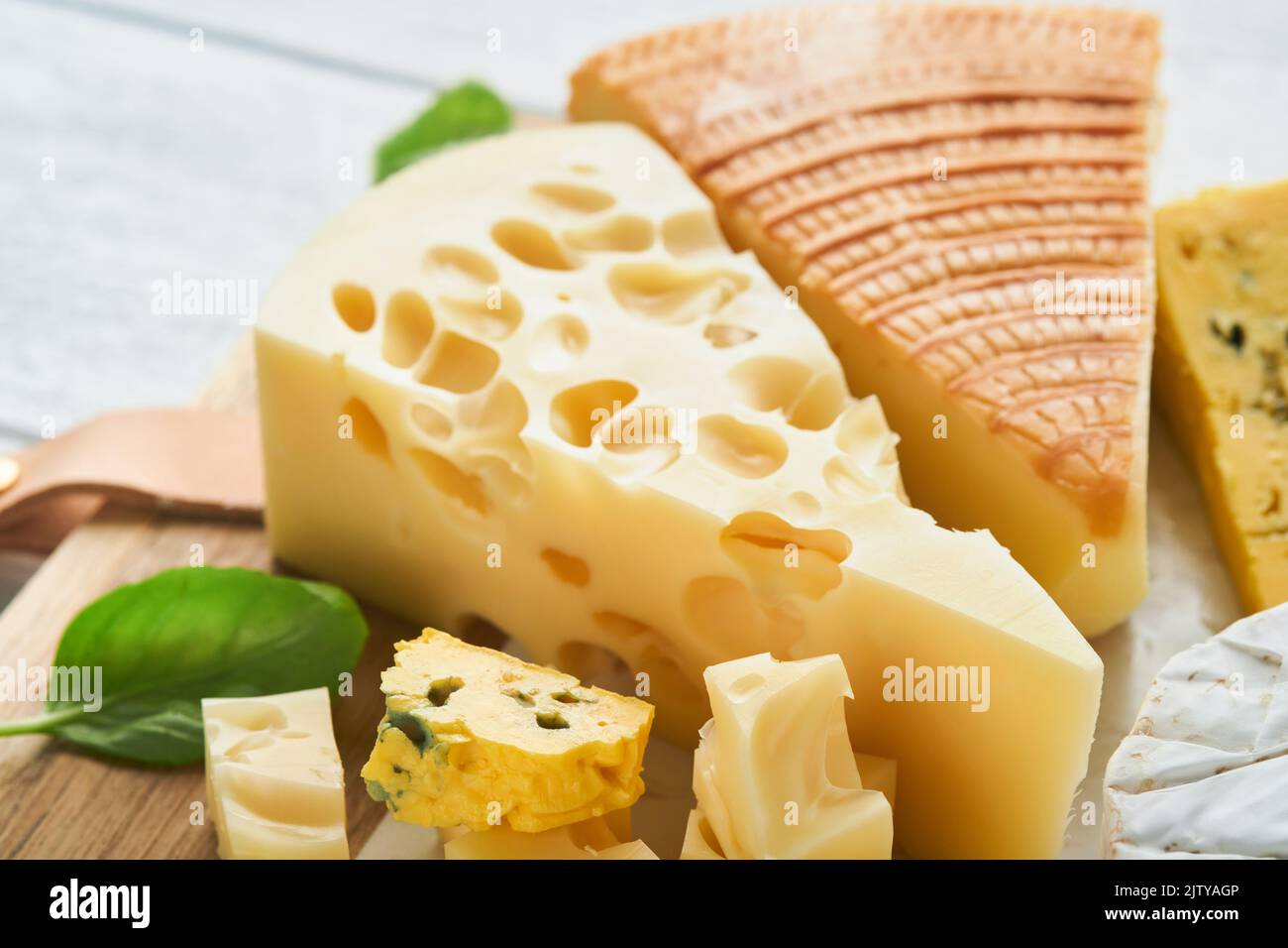 Morceau de maasdam et de camembert, fromage fumé, fromage bleu, parmesan, brie au basilic et poivre sur plateau de marbre blanc vieux bois Banque D'Images