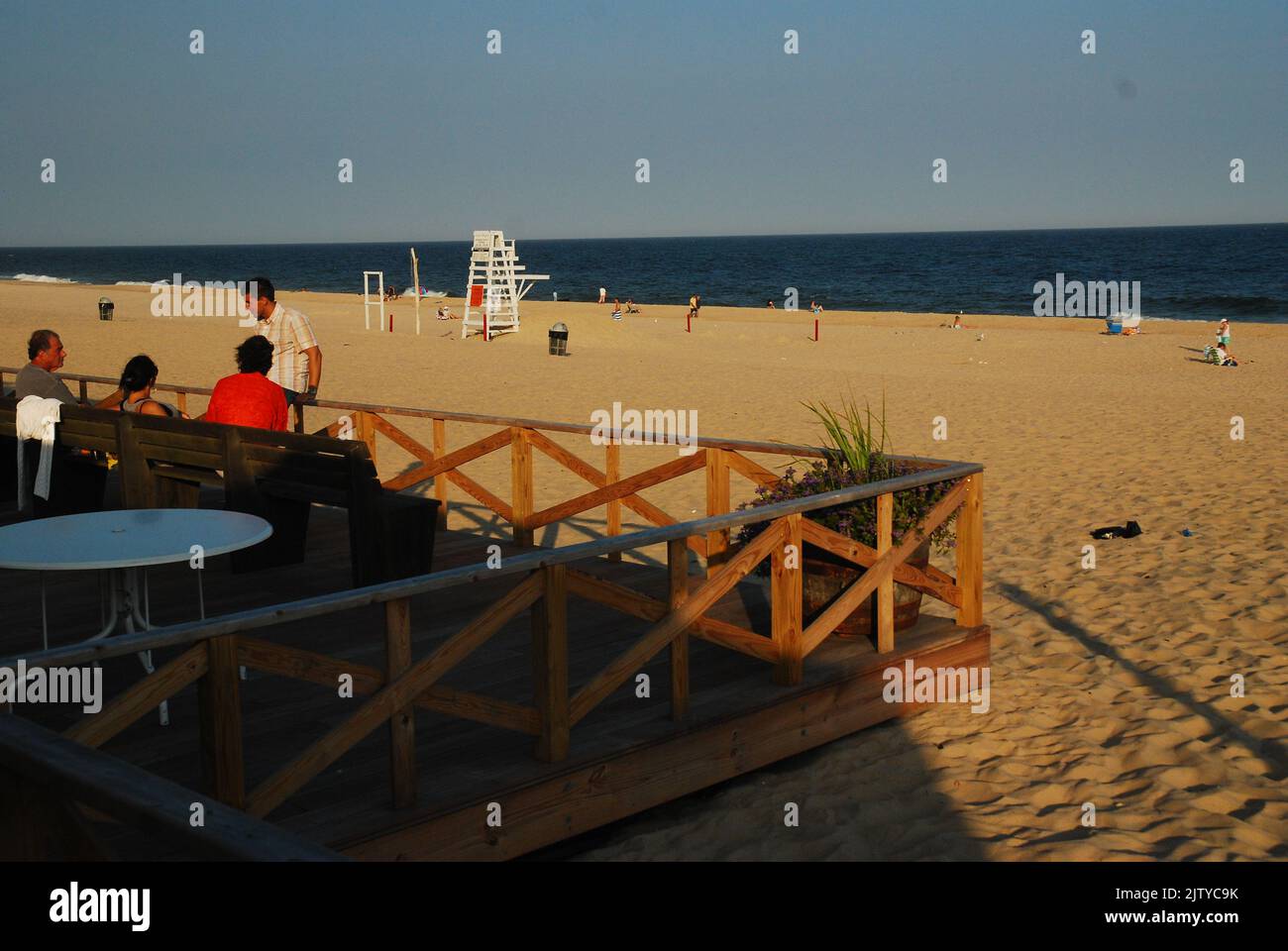 Un groupe de cinq s'assoient sur un banc et se balusent en fin d'après-midi tandis que la plupart de la plage se dégage un jour de vacances d'été Banque D'Images