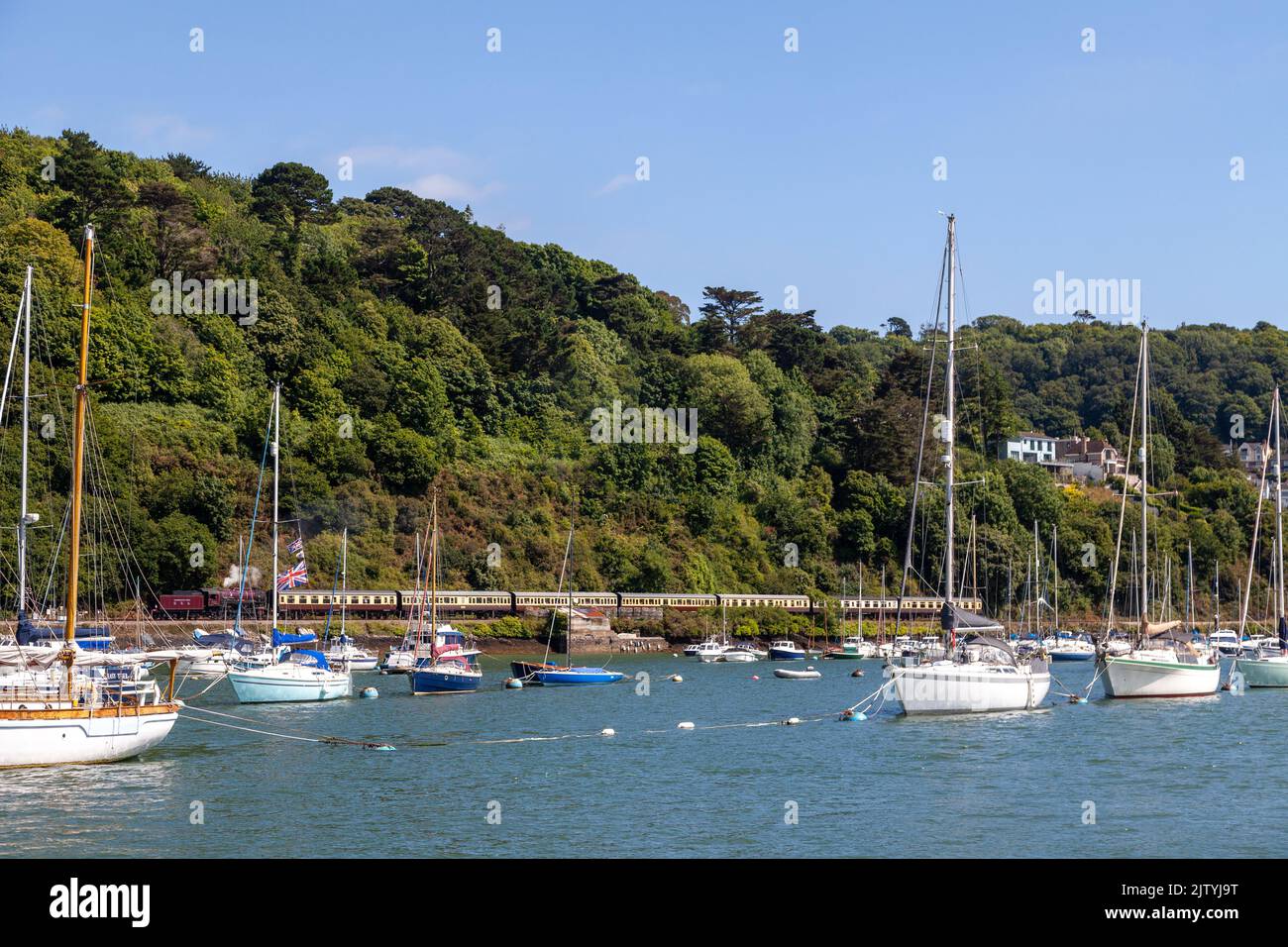 Ligne de chemin de fer du patrimoine de Dartmouth avec un train à vapeur longeant la rivière Dart et les bateaux amarrés en premier plan. Banque D'Images