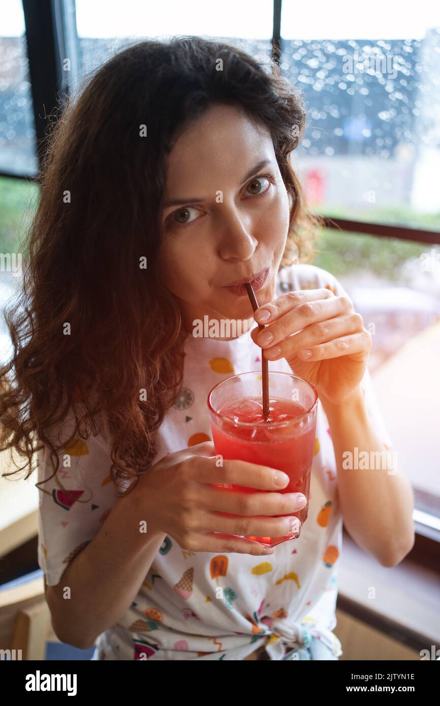 souriant et joyeux, une femme boit du jus de fruits aux baies avec du soda au café Banque D'Images