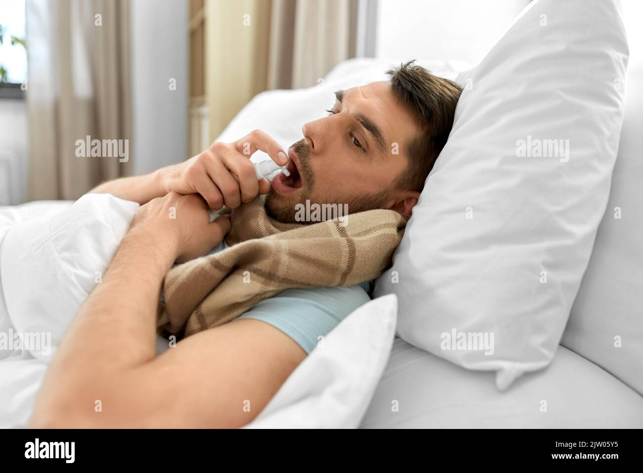 homme malade avec un spray oral couché dans le lit à la maison Banque D'Images