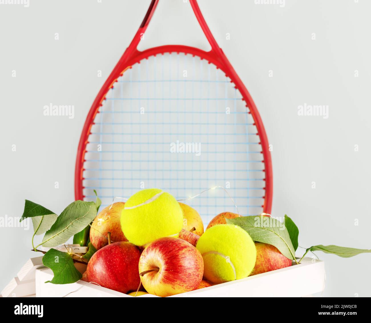 Composition de tennis avec balles de tennis jaunes, pommes dans une boîte en bois blanc avec éclairage et raquette de tennis rouge sur fond bleu. Concept de Healt Banque D'Images