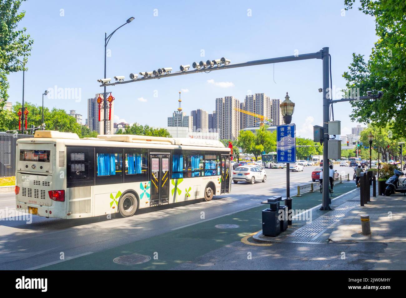 Un bus urbain vous conduira dans une avenue du centre-ville. Le véhicule de transport de passagers passe sous une structure métallique avec des feux et des caméras. Banque D'Images