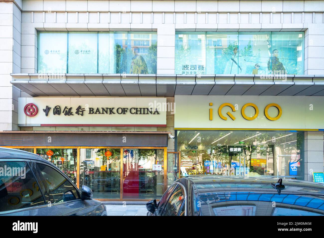Signes de la Banque de Chine et d'Iqoo. Les entrées d'affaires sont encadrées par des voitures modernes stationnées de l'autre côté de la rue. Banque D'Images