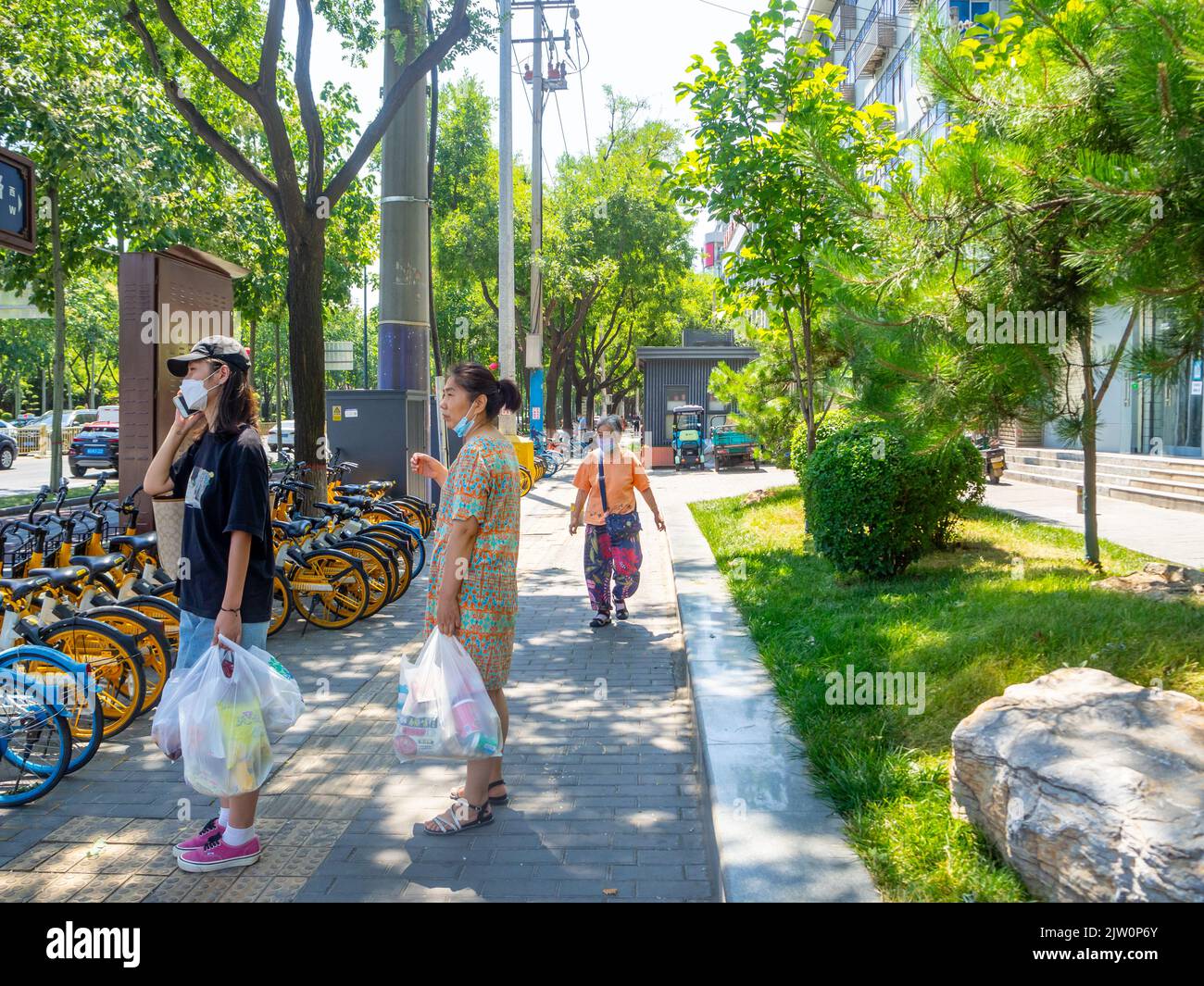 Les Chinois qui ont des sacs marchent sur un trottoir de la ville où se trouve un système de partage de vélos. Banque D'Images