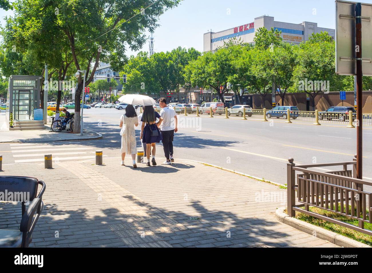 Les Chinois marchent sur un trottoir dans le quartier du centre-ville. L'un d'eux est doté d'un parapluie pour la protection contre les rayons UV. Banque D'Images