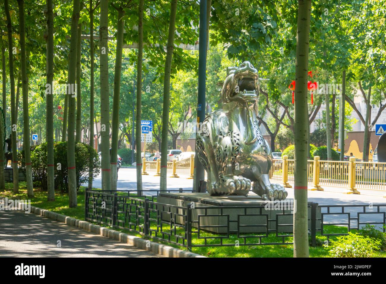 Une sculpture d'un lion d'argent décore une avenue médiane. La statue traditionnelle chinoise est entourée de magnifiques arbres. Banque D'Images