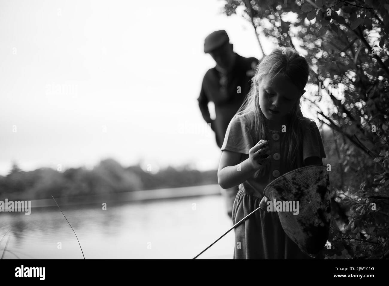 Une jeune femme caucasienne tient un filet de pêche et examine quelque chose dans une autre main tandis que son grand-père regarde en arrière-plan. Banque D'Images