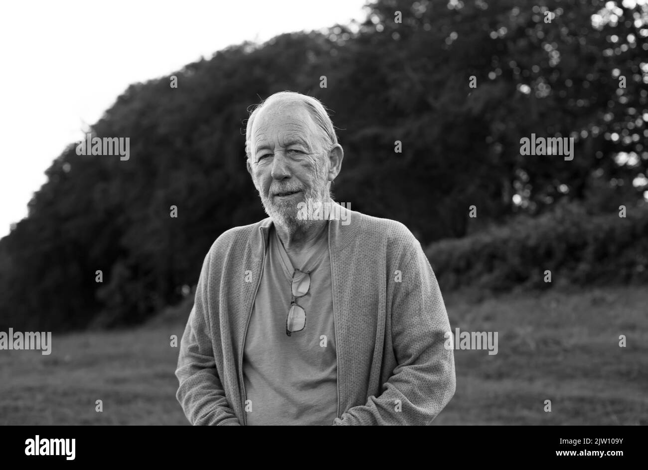 Un vieil homme debout dans un champ qui regarde la caméra avec un éclairage naturel. Banque D'Images