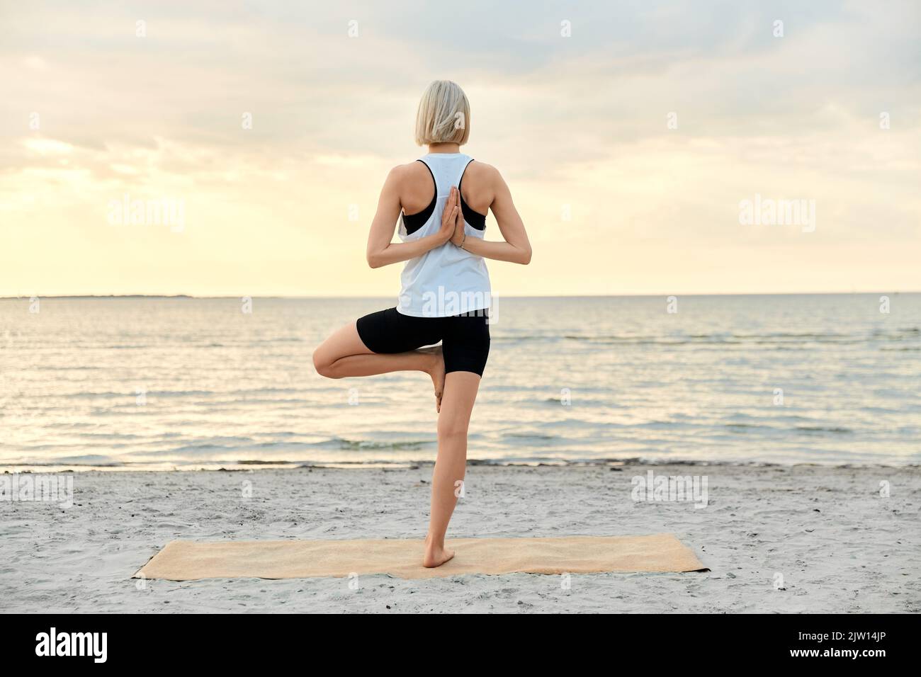 femme faisant de l'arbre de yoga pose sur la plage au coucher du soleil Banque D'Images