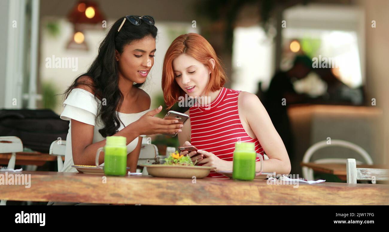 Filles attrayantes au restaurant, ami montrant l'écran à la petite amie femelle Banque D'Images