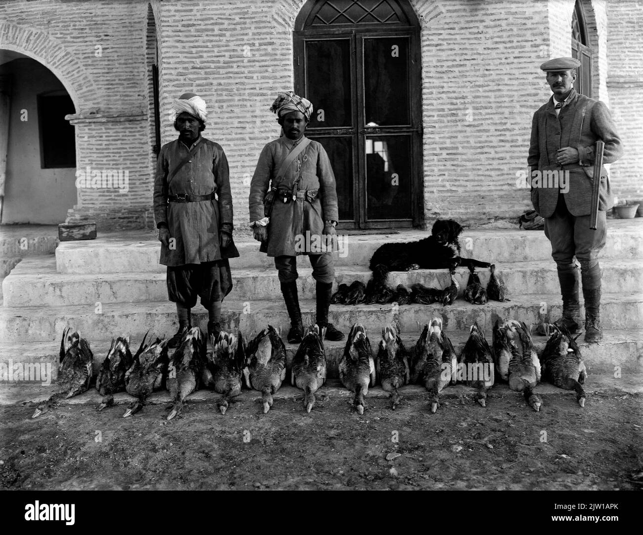 AJAXNETPHOTO. 1919-1920S (ENVIRON). INDE. FRONTIÈRE DU NORD-OUEST. - UN SAC DE JOUR - UN GENTLEMAN EUROPÉEN AVEC FUSIL DE CHASSE (À DROITE) EN TENUE DE CHASSE, UN CHIEN ET DEUX SCOUTS ÉVENTUELLEMENT EN ROBE DE WAZIRISTAN, AVEC LEURS OIES SAUVAGES ET LEURS TROPHÉES DE CANARD DISPOSÉS SUR LES MARCHES DU BÂTIMENT À L'ARRIÈRE. PHOTOGRAPHE:INCONNU © IMAGE NUMÉRIQUE COPYRIGHT AJAX VINTAGE PICTURE LIBRARY SOURCE: AJAX VINTAGE PICTURE LIBRARY COLLECTION REF:1920 4 2 Banque D'Images