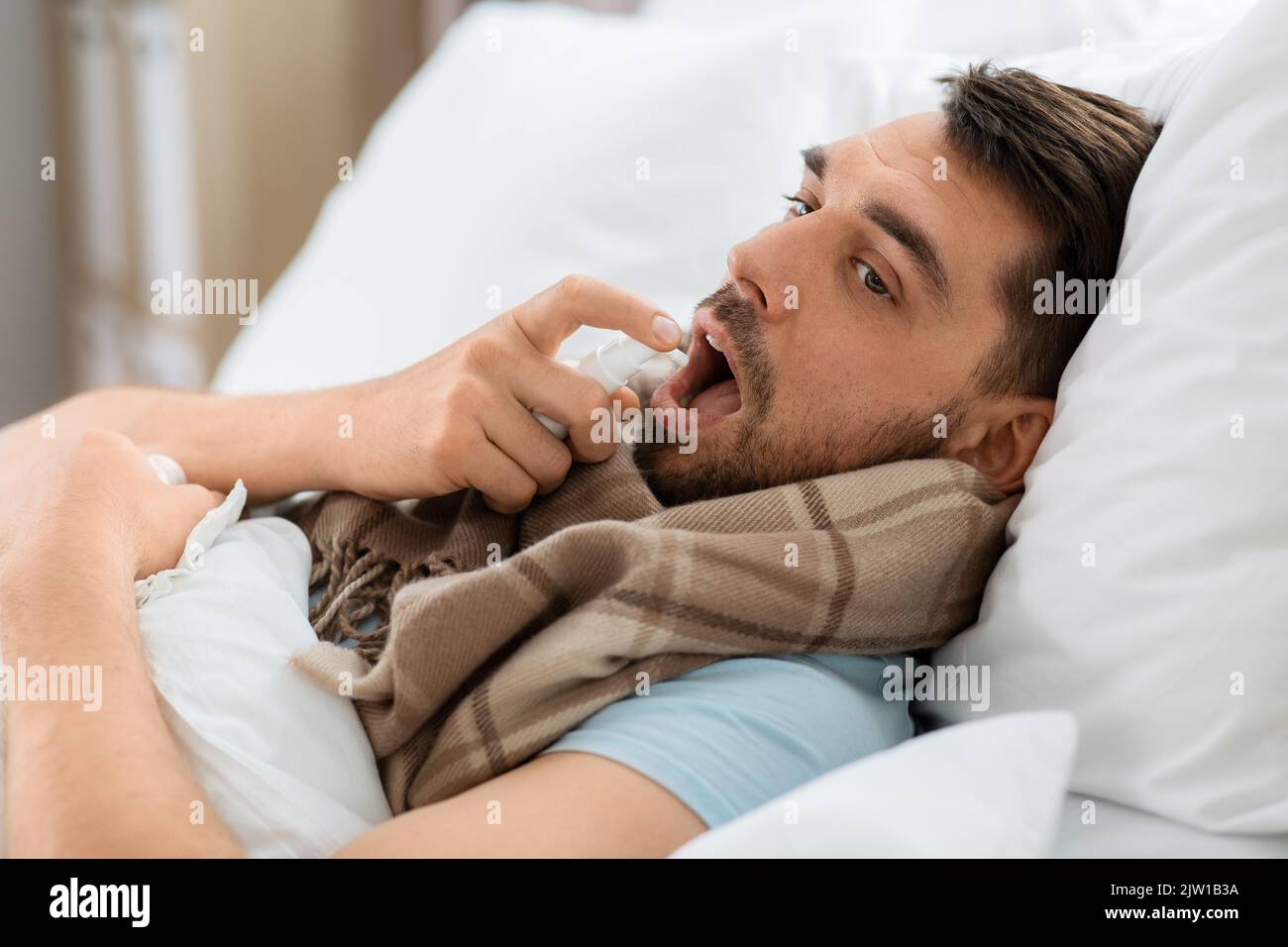 homme malade avec un spray oral couché dans le lit à la maison Banque D'Images