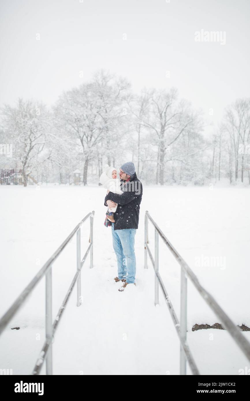 Un père de 30 ans caucasien tient bébé sur un pont dans la neige. Banque D'Images