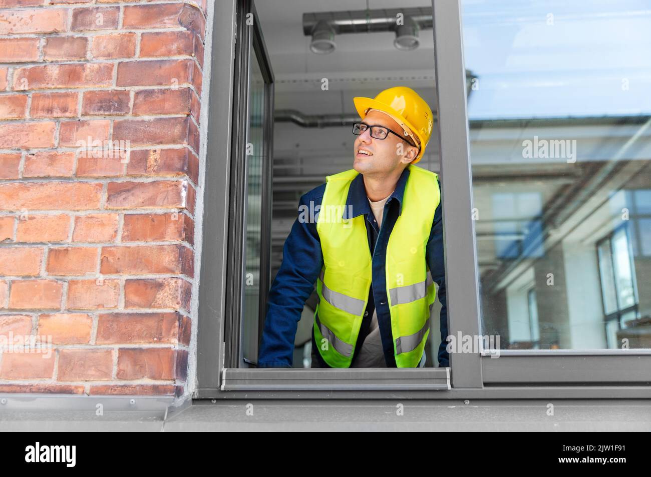 homme souriant constructeur dans le casque regardant par la fenêtre Banque D'Images