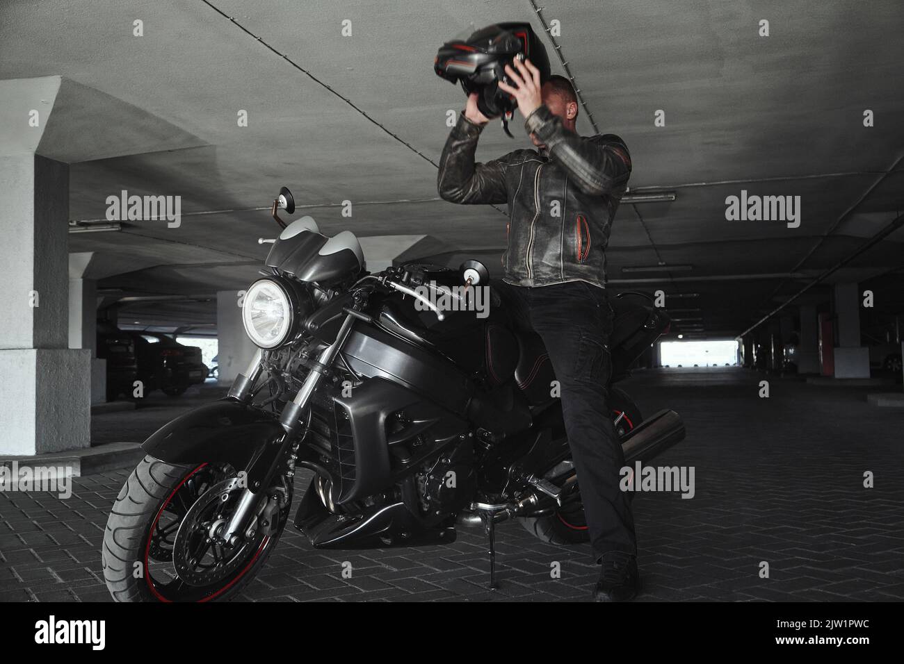 Un homme assis sur une moto prend son casque dans un garage souterrain, en mouvement Banque D'Images