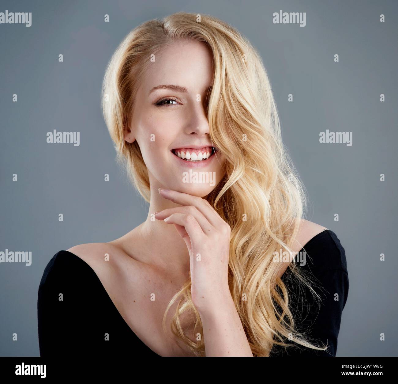 Une confiance qui correspond à sa beauté. Studio portrait d'une jeune femme attrayante avec de beaux cheveux blond longs posant sur un fond gris. Banque D'Images